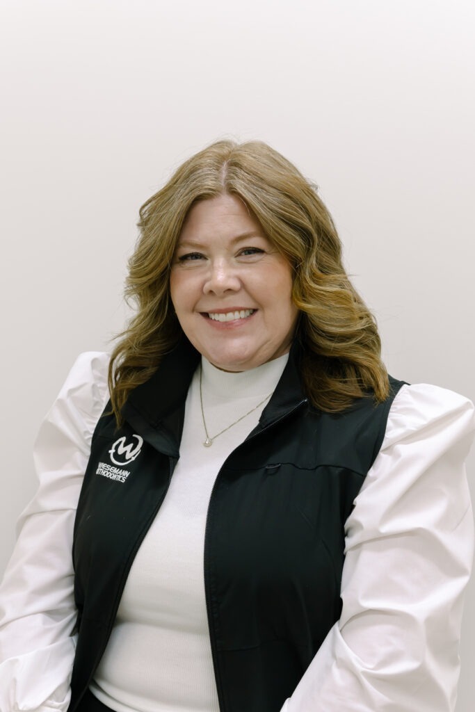Tina, receptionist at Wiesemann Orthodontics, smiling in a black vest with logo, showcasing friendly service for orthodontics in Russellville, KY.